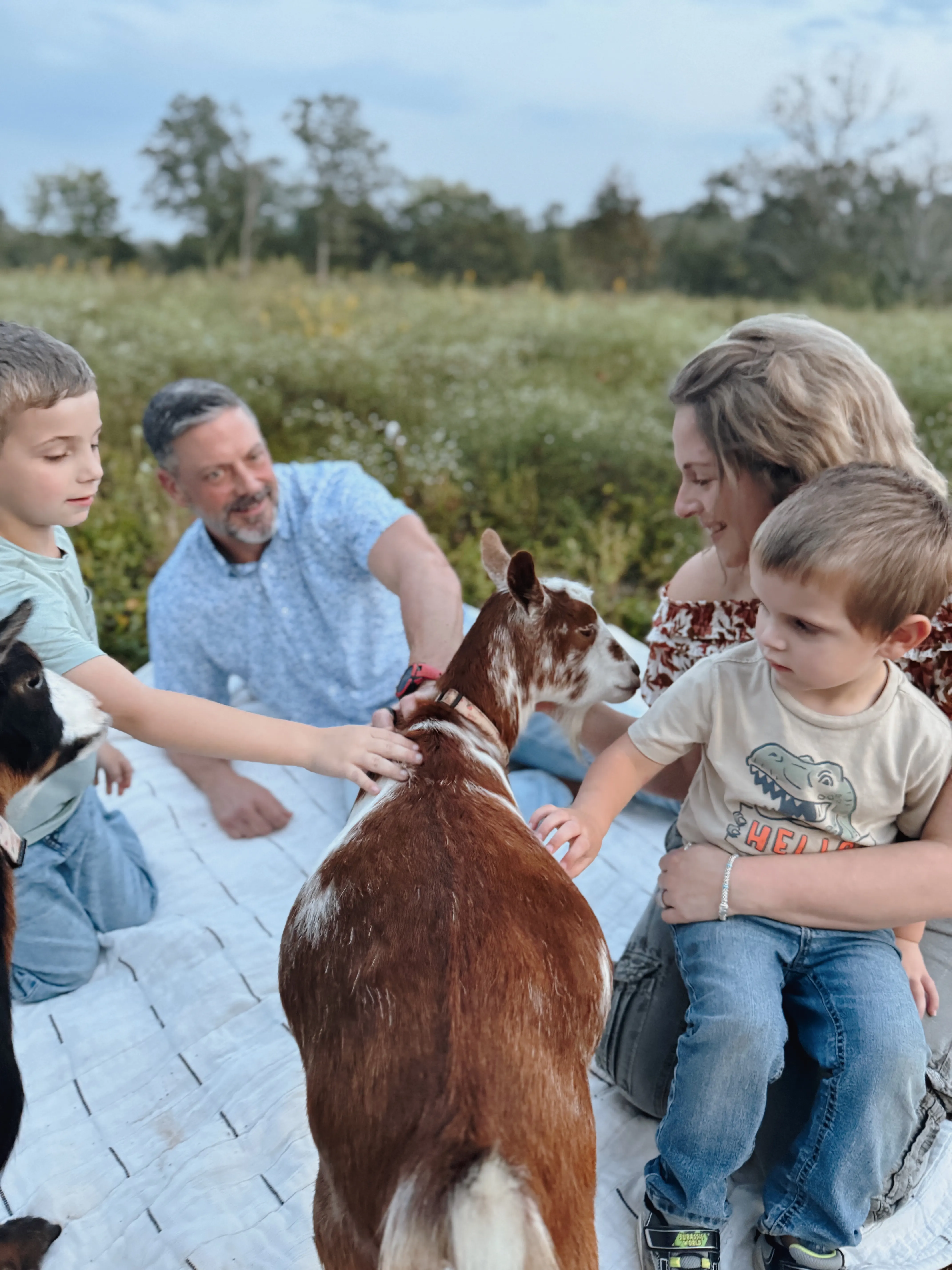Family with baby goats on a picnic blanket at golden hour at Magnolia Hill